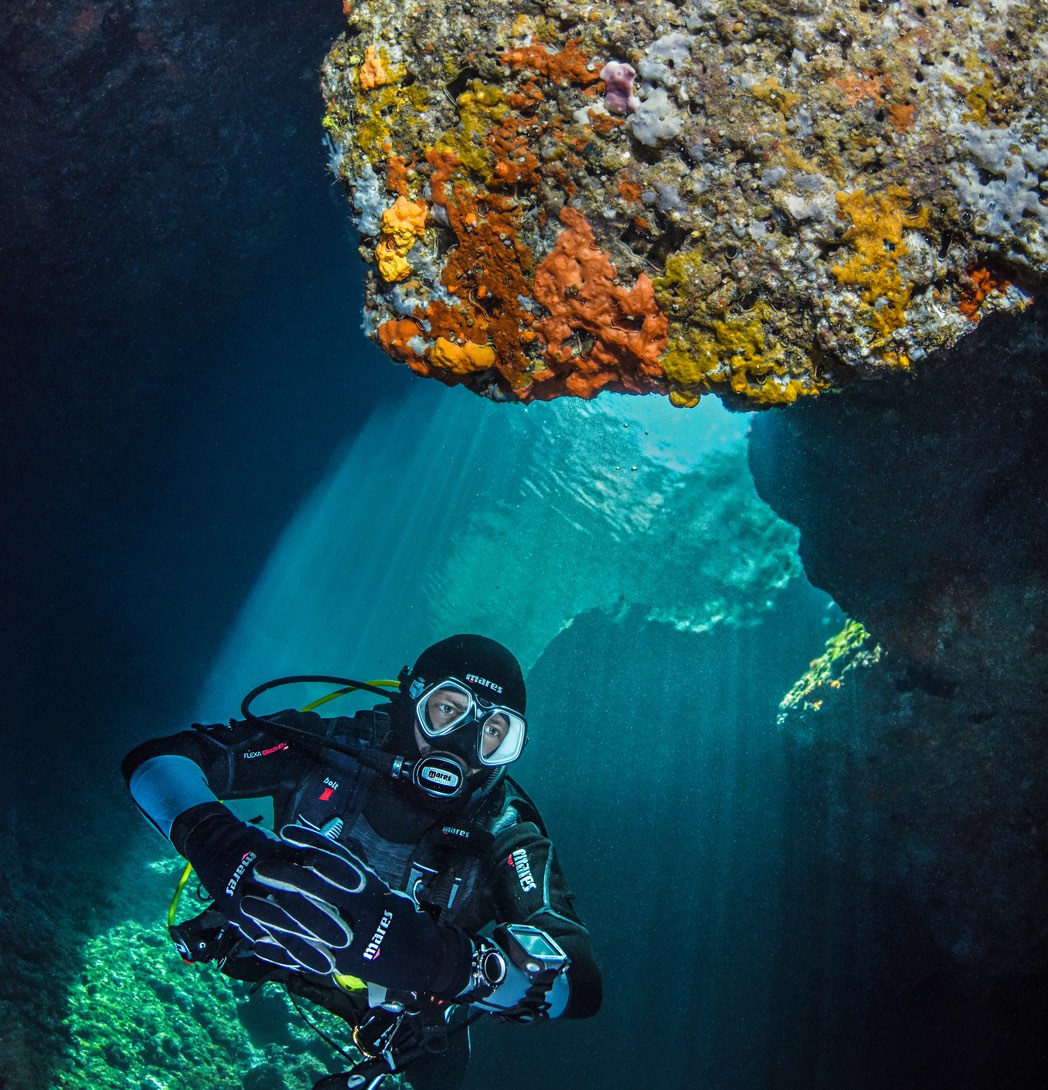 scuba diver swimming through rocky grotto looking nat the colourful marine life