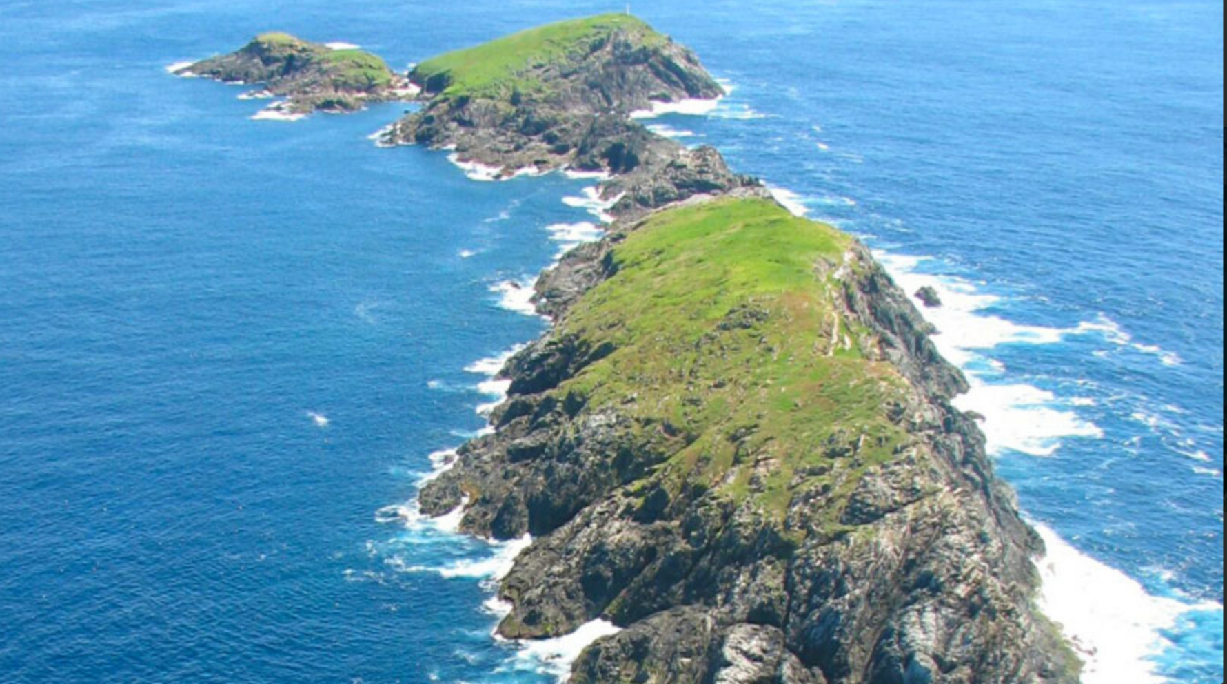 Island with rocky terrain and grassy areas surrounded by blue water