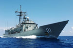 A gray boat with a helicopter on the deck, traveling on blue water with a clear sky in the background.