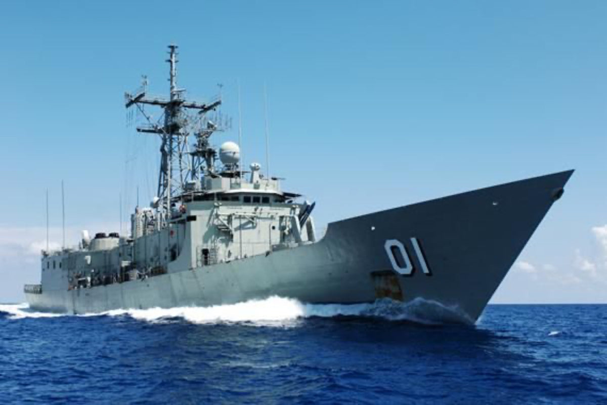 A gray boat with a helicopter on the deck, traveling on blue water with a clear sky in the background.